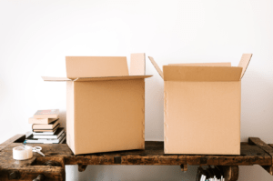 two cardboard boxes next to a stack of items and packing tape