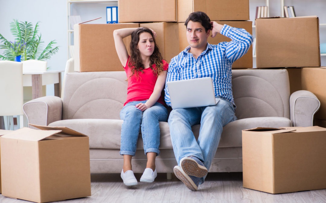 young couple on couch surrounded by moving boxes wondering if they should hire professional movers