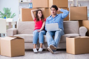 young couple on couch surrounded by moving boxes wondering if they should hire professional movers