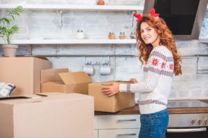 happy young woman in antlers headband unpacking cardboard boxes with tips for moving during the holidays