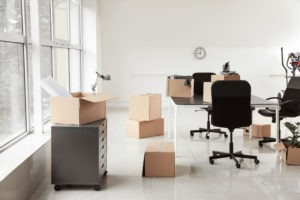 Cardboard boxes with belongings and furniture in new office on moving day for corporate moves