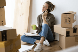 woman sitting next to moving boxes on the phone with a moving company to get moving quotes